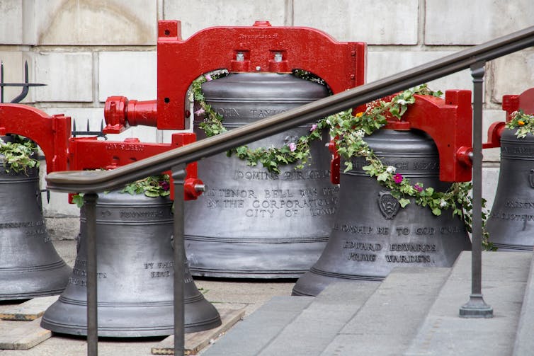 Large metal bells with red fixtures on the pavement.