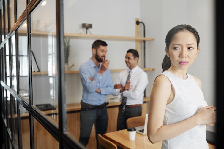 Two men in business attire chat while a woman in a sleeveless white top listens in, looking concerned.