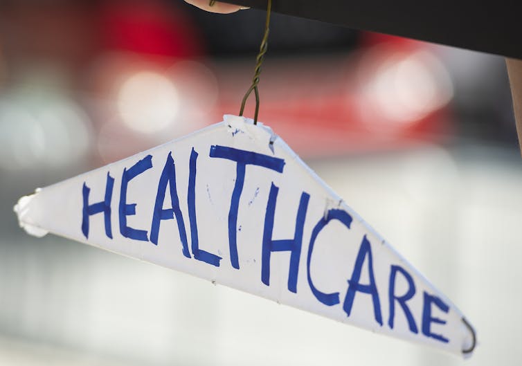A wire coat hanger with a paper banner that reads 'health care.'