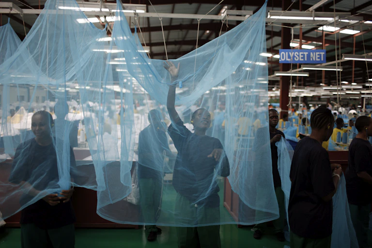 A woman stands inside a mosquito net in a factory setting