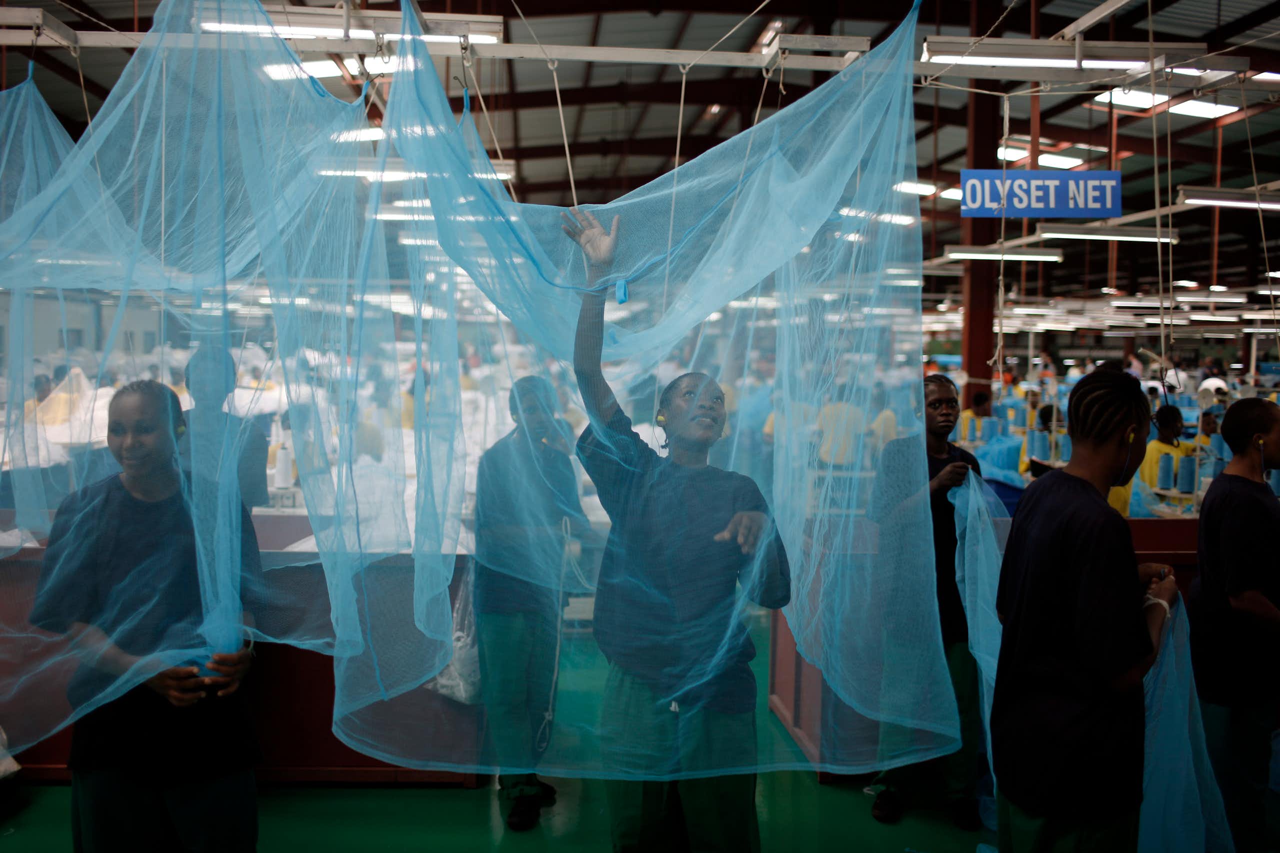 A woman stands inside a mosquito net in a factory setting