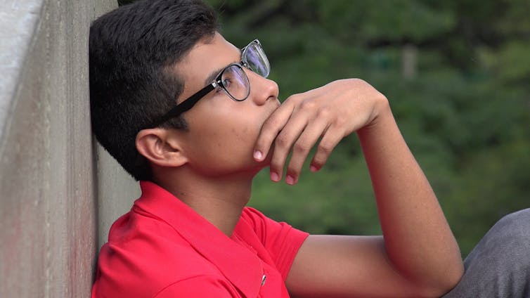 Pensive teenage boy in glasses sat with back to wall