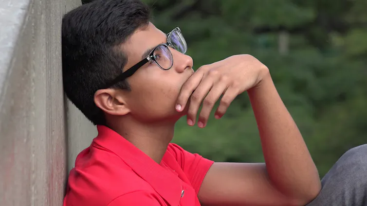 Pensive teenage boy in glasses sat with back to wall