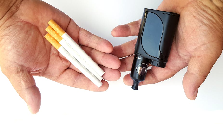 A person holds three cigarettes in one hand and a disposable vape in the other hand.