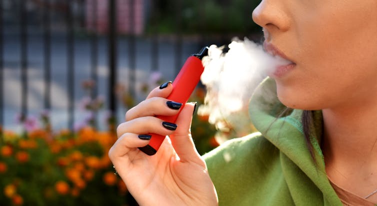 A young woman breathes out vapour from her vape pen.