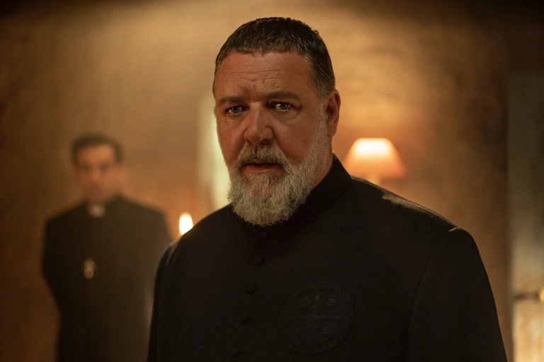 Russell Crowe in all black, with a priest stood behind him.