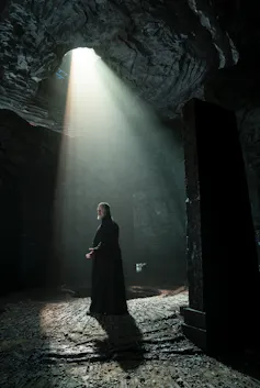 Russell Crowe in priest's black robes, stood under a spotlight.