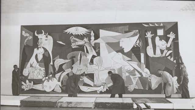 Cinco hombres colocan el cuadro de Guernica en la pared.