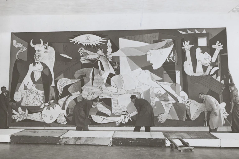 Cinco hombres colocan el cuadro de Guernica en la pared.