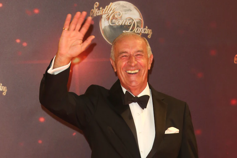 Goodman waves wearing a black tuxedo.