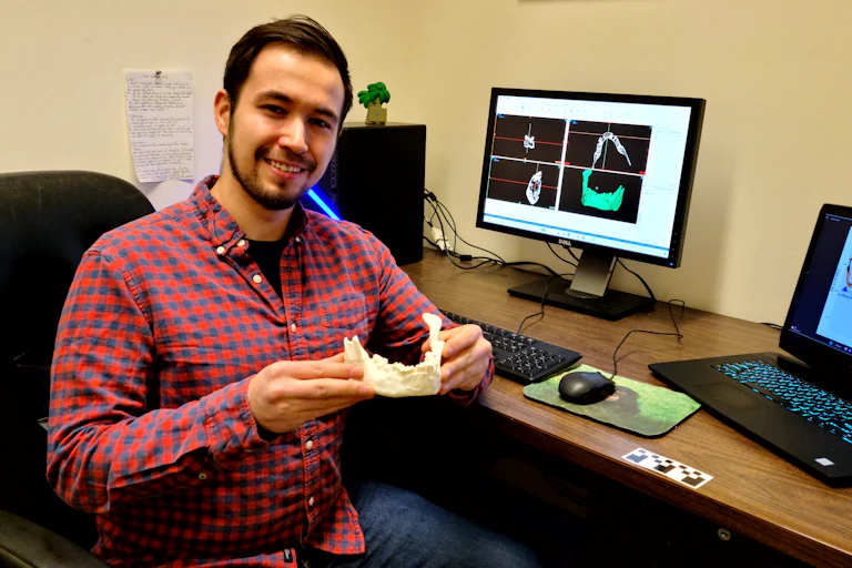 man seated at desk holds white model of jawbone