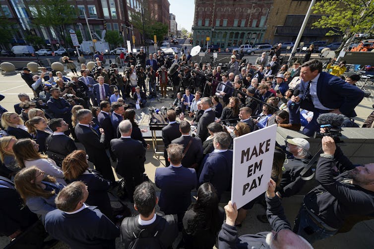 A large crowd of people surrounding a small group of people on a public plaza.