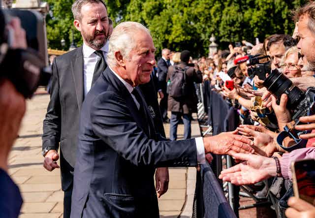 King Charles shaking hands of members of the public across a fence
