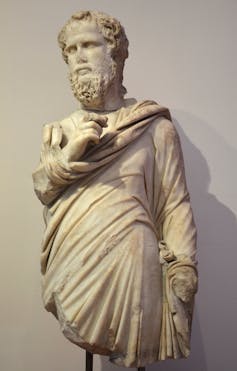 A marble statue of a bearded man with curly hair in a toga-like garment.