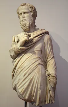 A marble statue of a bearded man with curly hair in a toga-like garment.
