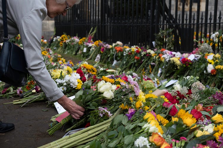 A woman lays a bouquet into a pile of flowers outside of Buckingham Palace