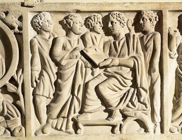A bone-colored carving of five men in toga-like garments, with one holding a tablet.