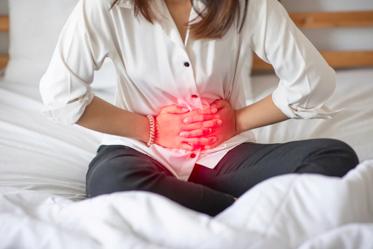 femme sur son lit se tient le ventre de douleur