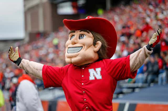 Mascot wearing red cowboy hat and red shirt spreading his arms.