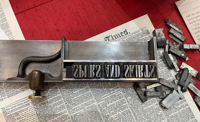 Text of a Victorian newspaper seen that says 'Times' and features letters laid out in an old-fashioned letter press box.