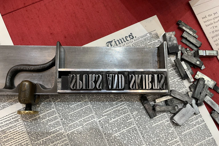 Text of a Victorian newspaper seen that says 'Times' and features letters laid out in an old-fashioned letter press box.