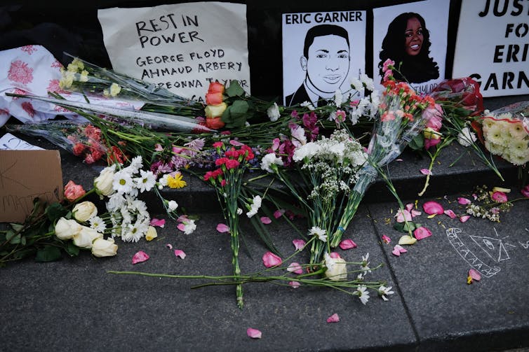 Flowers lay on the ground before hand-drawn images of people killed by police and notes listing their names.
