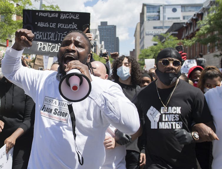 Two black men lead a march down a street. One of them chants into a megaphone.