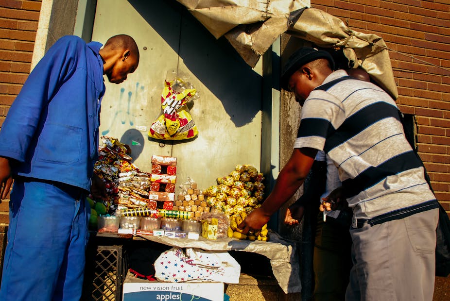 Two men eye good at an informal stall displaying snacks. 