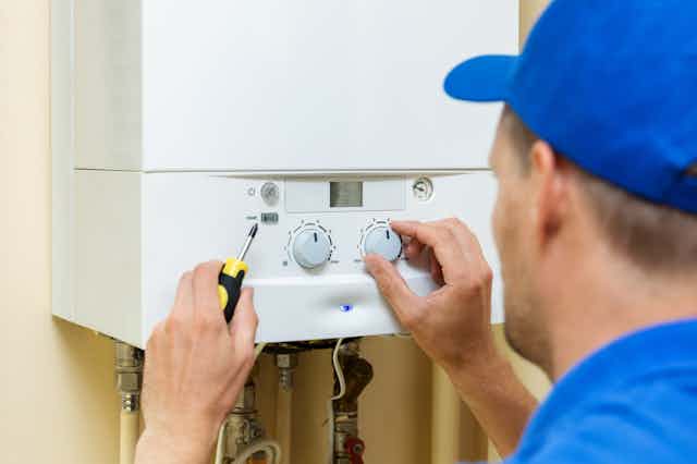An engineer in blue cap and shirt adjusts the dial on a boiler.