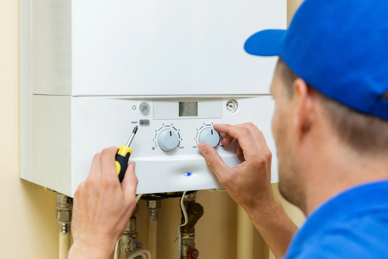 An engineer in blue cap and shirt adjusts the dial on a boiler.
