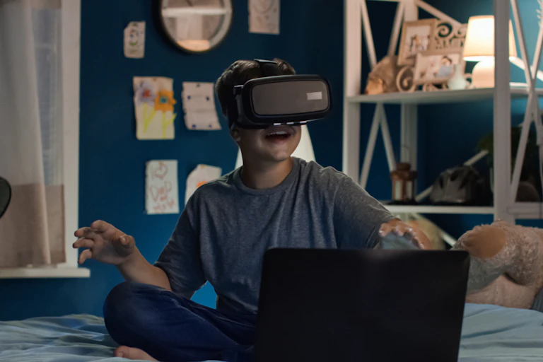 Boy in bedroom with laptop using VR headset
