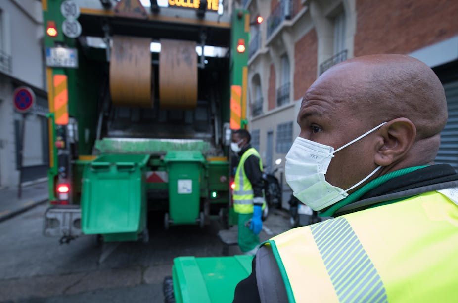 Des éboueurs du service de nettoyage de la municipalité de Paris "Proprete de Paris", portant des masques, collectent des poubelles dans un camion à ordures à Paris le 30 avril 2020.