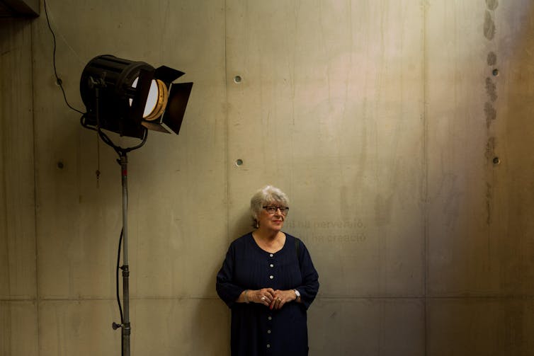 Katinka Farago leaning on a concrete wall under a large staging light.