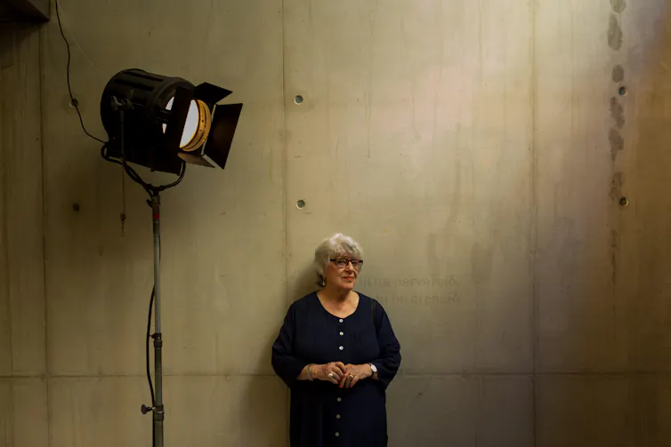 Katinka Farago leaning on a concrete wall under a large staging light.