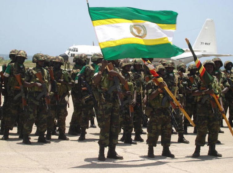Soldiers carry the flags of the African Union and Uganda next to a plane.