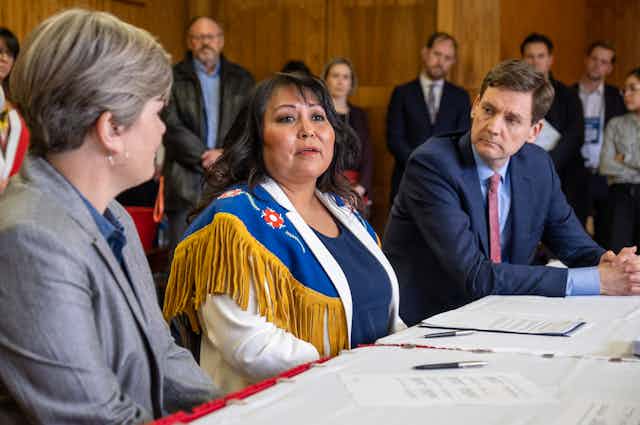 An Indigenous woman sitting at a table in between two other people with documents and pens on the table.