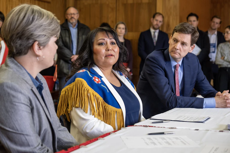 An Indigenous woman sitting at a table in between two other people with documents and pens on the table.