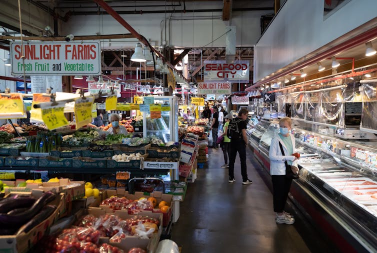 People seen with grocery carts in a produce section near a fish section.