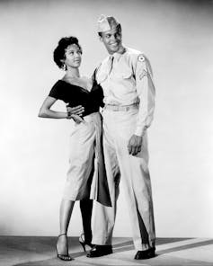 A black man dressed in a military uniform stands next to a woman with her hand on her hip.