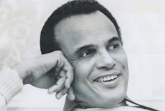 A black man is smiling as he looks into the distance.