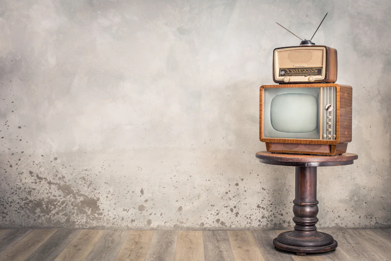 An old TV, set on a pedestal and old radio on top of the TV.