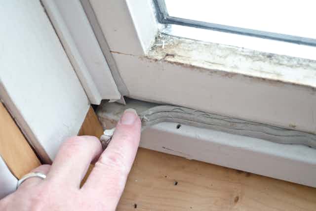 A hand presses in caulking on an old, draughty windowframe