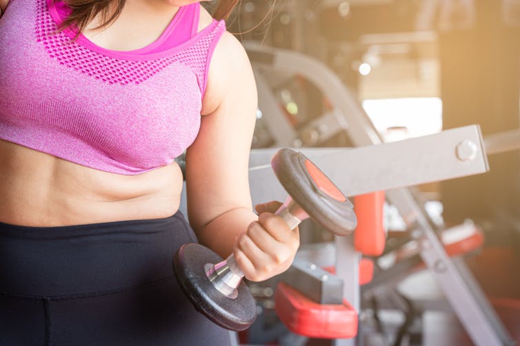 woman in gym setting holding dumbbell in one hand