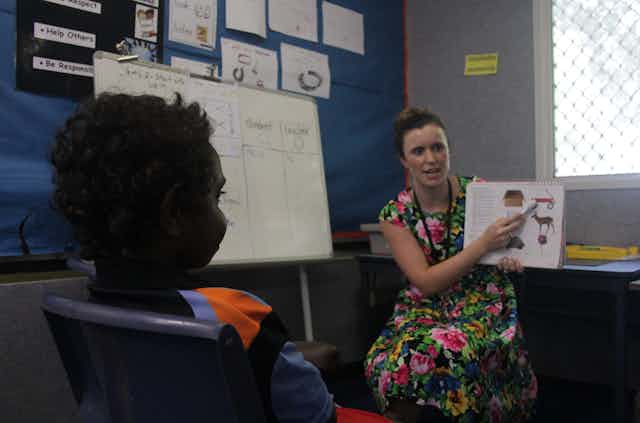 A young student listens to a teacher pointing to images in a book.