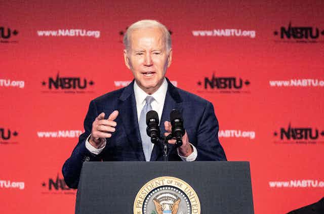 US president Joe Biden points to the audience while giving a speech behind a lectern.