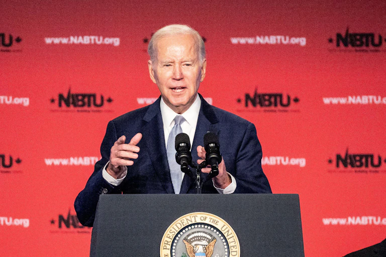 US president Joe Biden points to the audience while giving a speech behind a lectern.