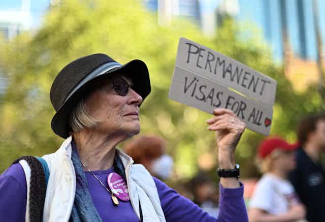 Woman holds placard saying "Permanent visas for all"