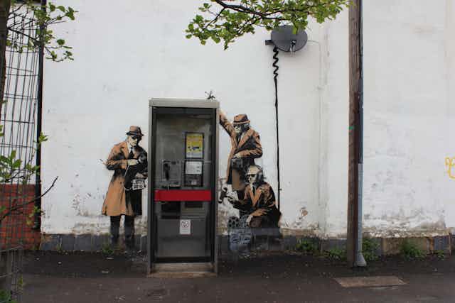 A piece of wall art showing three men in hats as spies next to a telephone booth.