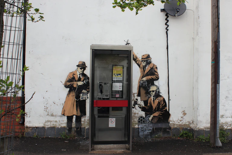 A piece of wall art showing three men in hats as spies next to a telephone booth.