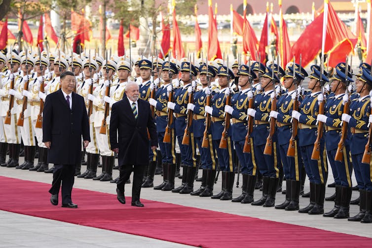 Xi Jinping and Lula da Silva walking on a red carpet past Chinese soldiers.